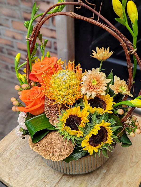 The Watering Can | Pincushion, sunflowers, orange roses, and bract mushrooms in a European style floral arrangement.