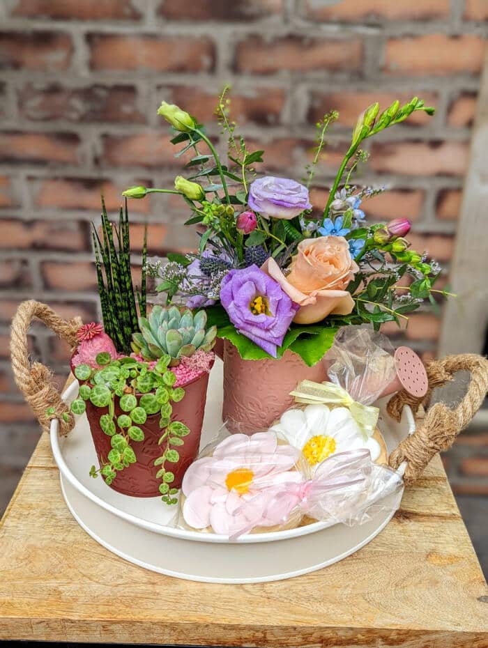 The Watering Can | A small European style arrangement and small planter with two flower sugar cookies on a tray.