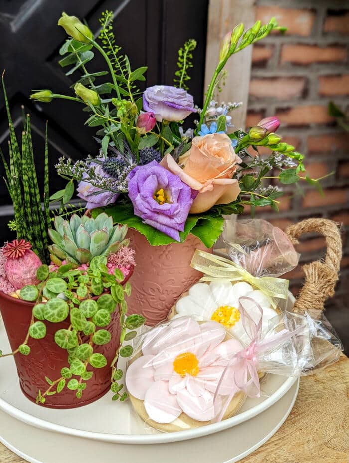 The Watering Can | Alternate view of a small European style arrangement and small planter with two flower sugar cookies on a tray.