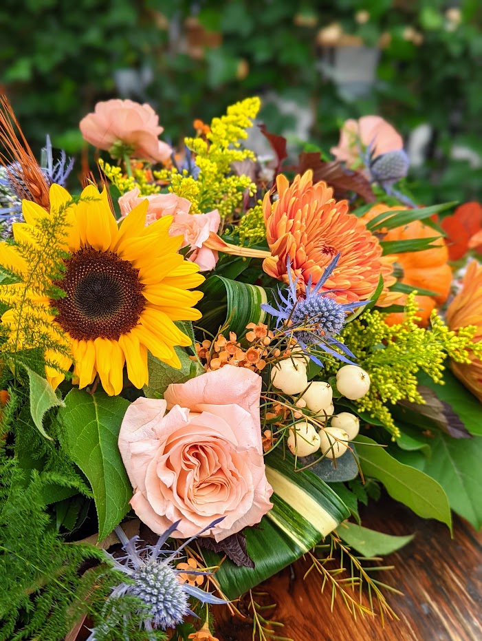 The Watering Can | Close up of sunflower, roses, hypericum, and thistle in a fall table centerpiece