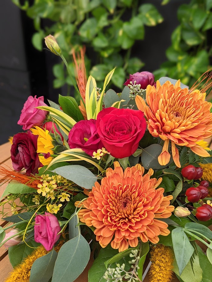 The Watering Can | A close up of orange mums, red lisianthus and burgundy hypericum in a table centerpiece