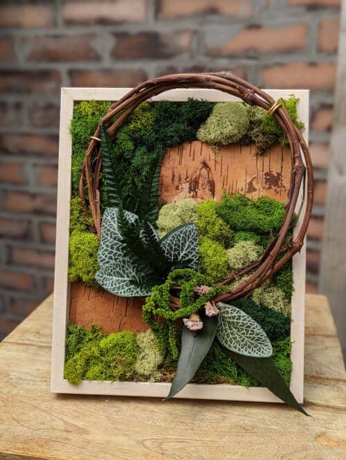 The Watering Can | A grape vine wreath accompanies an artful display of green mosses in a light wooden frame.