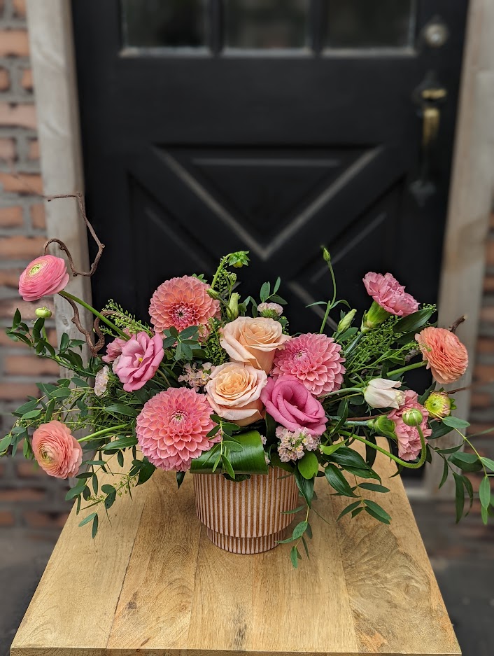 The Watering Can | Pink and peach dahlias, ranunculus, and roses explode out from a ribbed pink ceramic container.