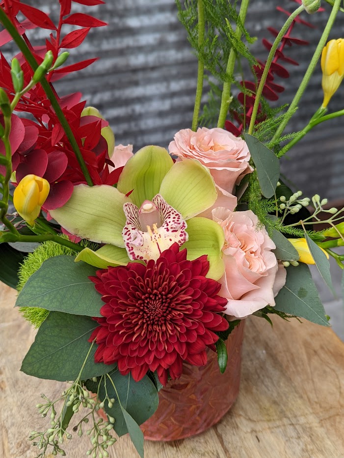 The Watering Can | A red mum, green cymbidium orchid bloom, and peach roses in a European style floral arrangement