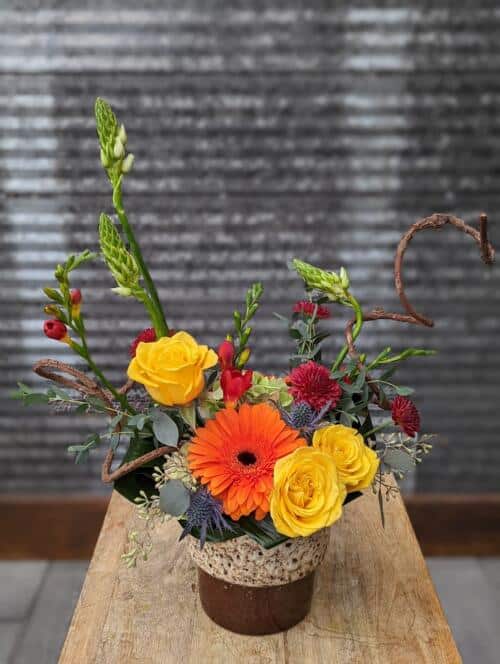 The Watering Can | A fall European arrangement in yellows, reds, and orange designed in a brown and cream ceramic container.
