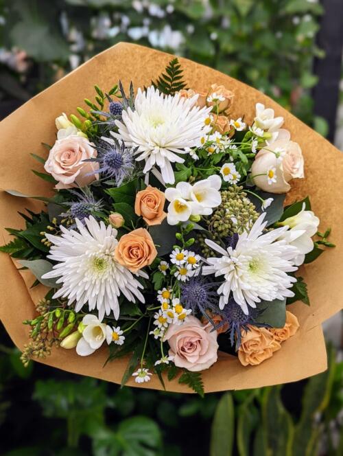A spring meadow look. Featuring white mums, purple thistle, toffee spray roses, fragrant freesia, chamomile and lush greenery.