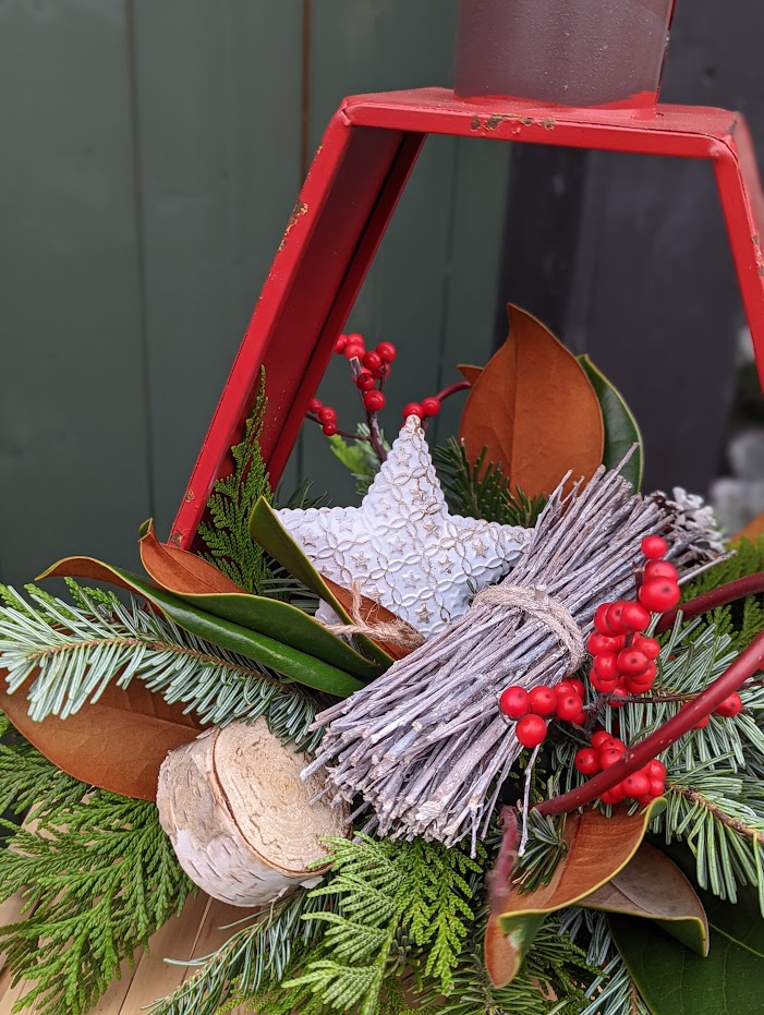 The Watering Can | A white tin star, whitewashed sticks, a birch lolly and red ilex berries in a festive arrangement designed in a red lantern.
