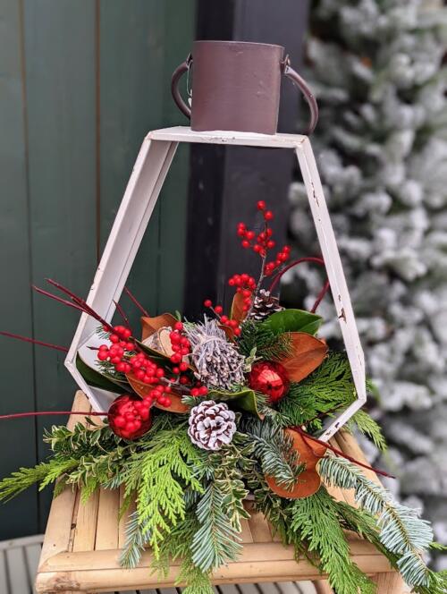The Watering Can | A winter festive arrangement with ornaments and pine cones designed in a white lantern.