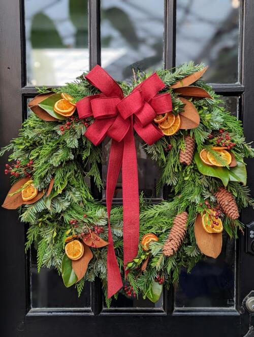 The Watering Can | An evergreen wreath with magnolia, orange slices and pine cones tied with a large red bow.
