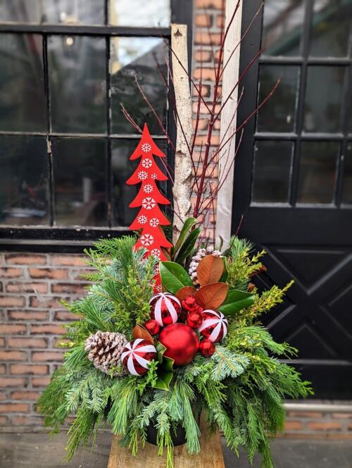 The Watering Can | An outdoor urn design with a red wooden tree and a cluster of red and white ornaments.