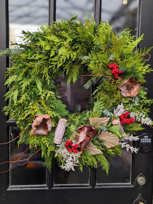 The Watering Can | A winter wreath decorated with red berries, white ruscus, and sparkling palm caps.