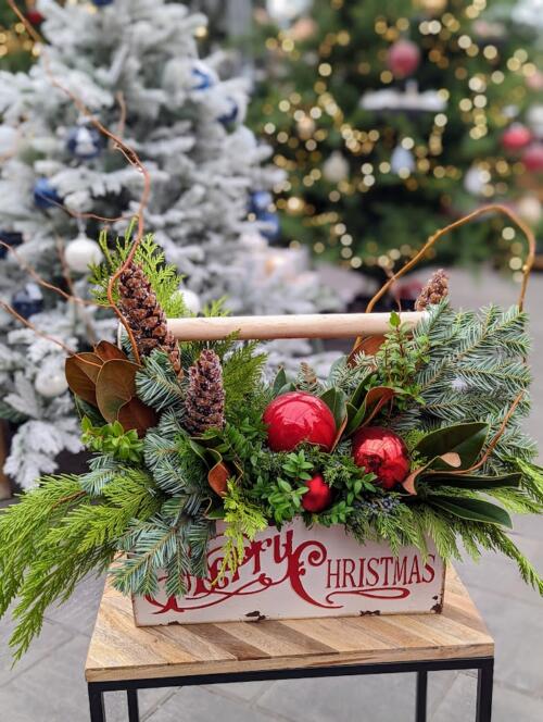 The Watering Can | A winter festive arrangement designed in a white tin toolbox with a wooden handle that reads "Merry Christmas" in red lettering.