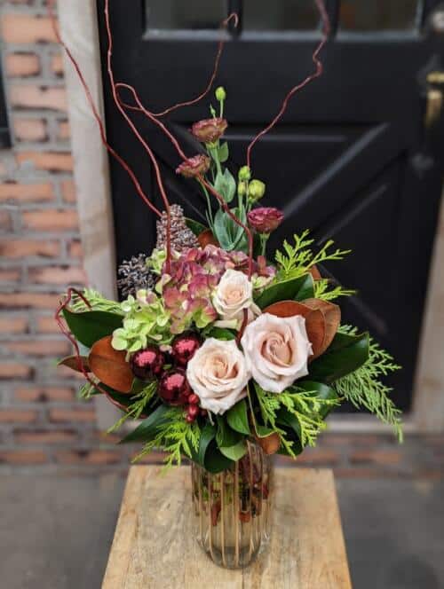 The Watering Can | A burgundy and blush winter bouquet in a tall, brown tinted glass vase.