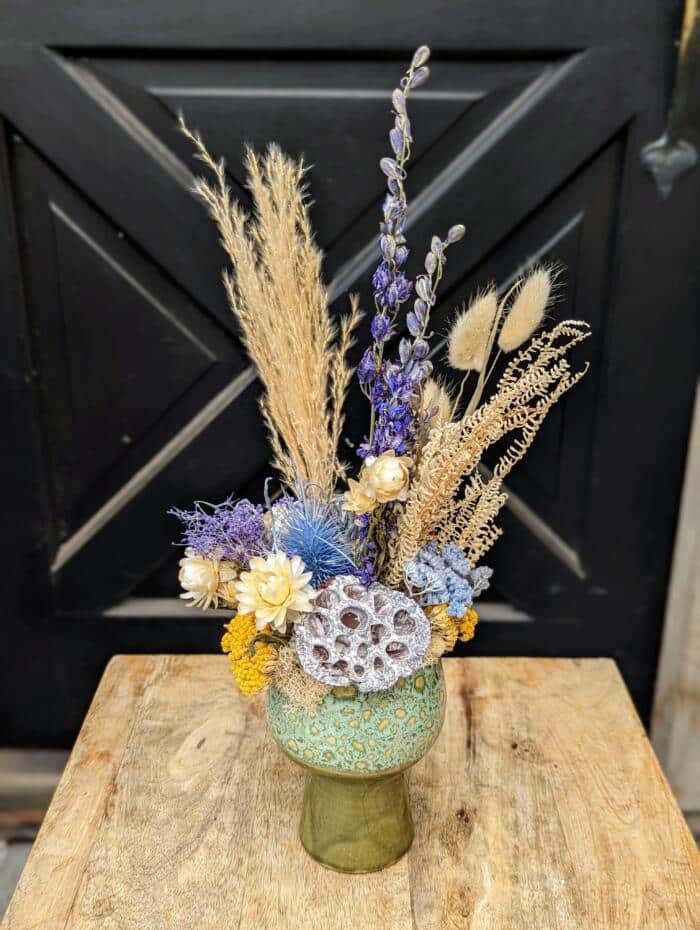 blue-green aged, pedestal ceramic. Featuring bursts of blue, yellow and neutral grasses and dried foliage.