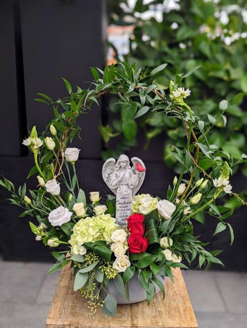 Grey round ceramic container with a wreath of italian ruscus. Sprouting white spray roses, white star of Bethlehem and white lisanthus. a pop of red roses, and draping coin eucalyptus.