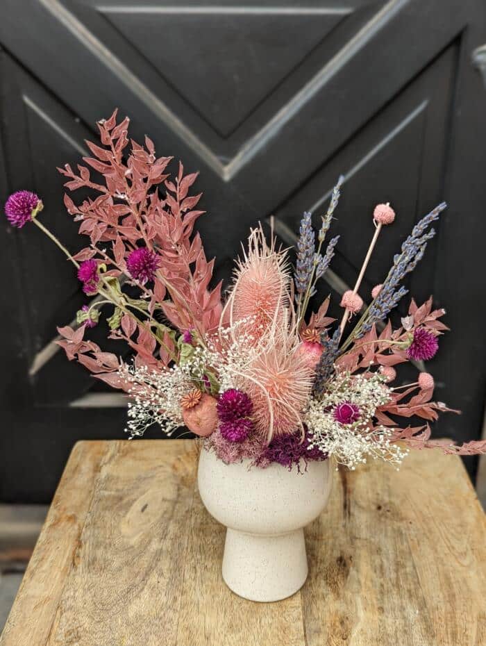 A soft pink tapered ceramic container. Filled with various pink dried blooms. Mixed textures and an asymmetrical setting