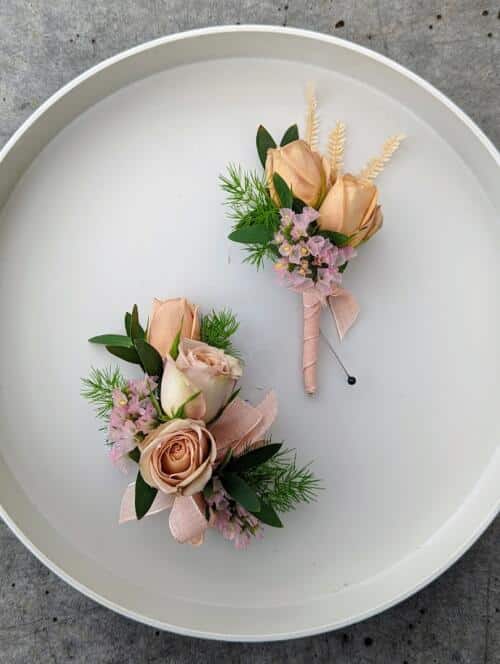 A boutonniereand corsage featuring blush pink spray roses, light pink statice and a variety of greenery.