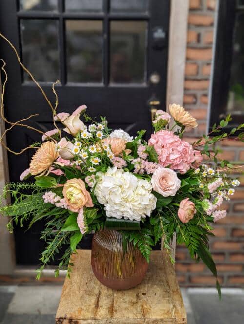 A pink tinted filled with white and blush hydrangeas, peach ranunculus, chamomile, peach mums, pale pink roses