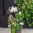 A large charcoal planter featuring a white orchid, white calla lily, prayer plant, variegated rubber tree. Mini white kalanchoe and cyclamen. Finished with reaching curly willow branches.