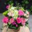 A light pink glass vase filled with green and pink blooms such as green hydrangea, hot pink roses and so much more to brighten your day.