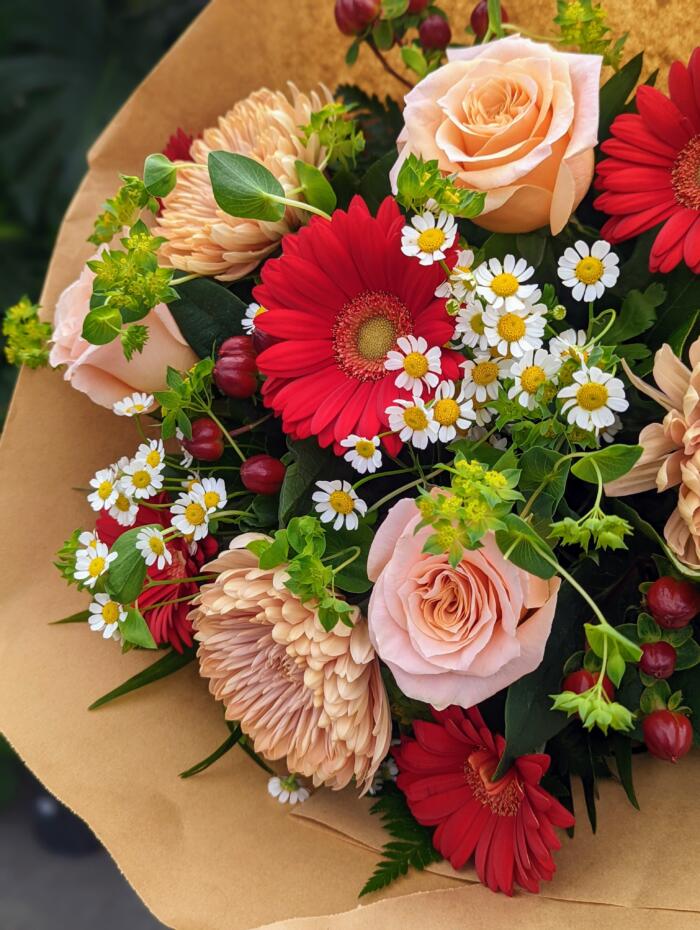 A bright and sweet bouquet of peach mums, peach roses, red mini gerberas, dainty chamomile and greenery.