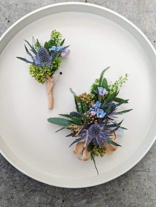A corsage and boutonniere with a thistle focal point, blue tweedia flowers and greenery.