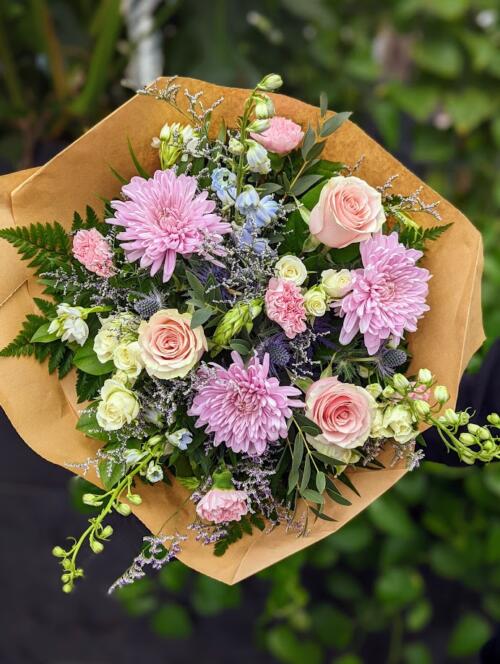 a pastel bouquet featuring lavender mums, pink roses, thistle, blue delphinum and more.