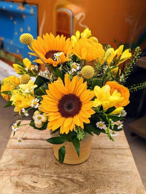A soft yellow ceramic filled with bright yellow blooms. Featuring large sunflowers, yellow ranunculus, frgrant yellow freesia, yellow craspedia and sprigs of chamomile and thlaspi.