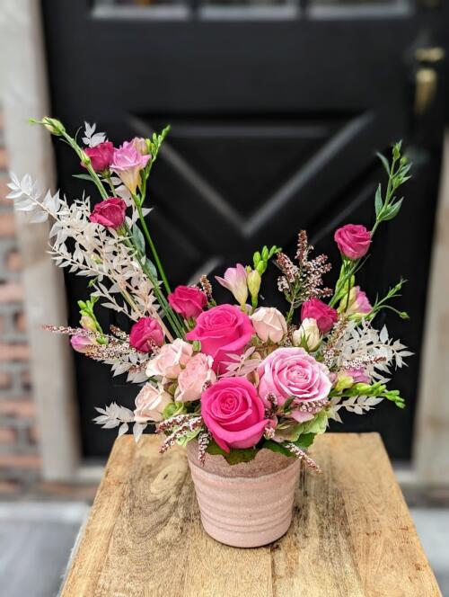 A soft pink ceramic overflwoing with asymmetrical pink blooms. including a collection of pink roses, pink freesia, pink lisianthus and dried pink ruscus.