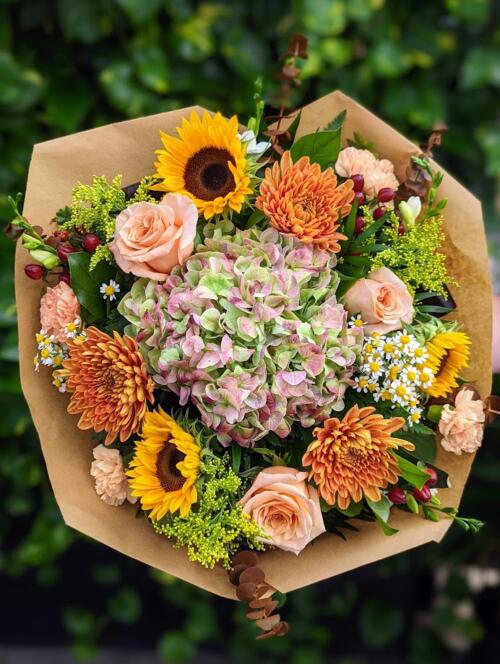 A large bouquet filled with summery/fall tones. featuring alarge antique hydrangea, sunflowers, deep orange mums, peach roses and more.