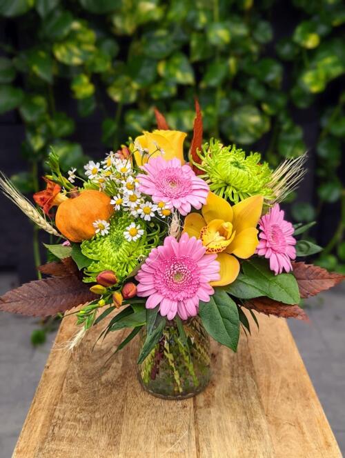 A clear quitled vase filled with bright autumn florals. light pink mini gerberas, yellow orchids, yellow roses, green mums and more