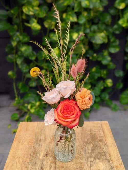 a small bud vase filledw ith fall florals. orange rose, blush spray roses, peach ranunculus,