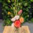 a small bud vase filledw ith fall florals. orange rose, blush spray roses, peach ranunculus,