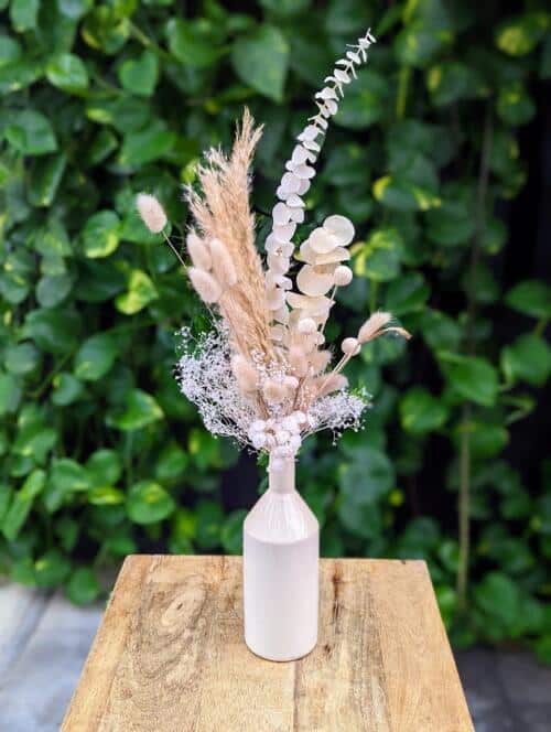 A white bottle filled with neutral dried florals.