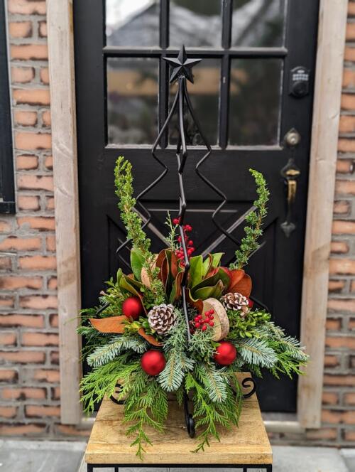 A black metal tree with a base filled with holiday greenery and red ornaments