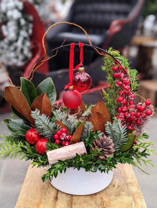 A white container with a black hoop durrounded by winter greenery, red berries and red hanging ornaments.