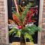 A dark glass vase filled with winter greenery, red berries and a red bell.