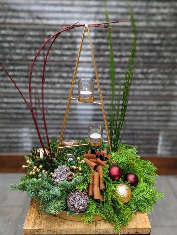 a large gold tree shaped tealight candle holder on a bed of holiday greenery accented with burgundy and gold ornaments