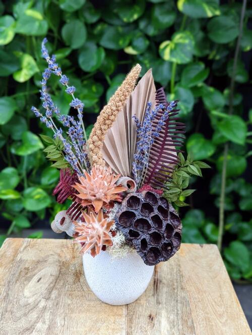 a white ceramic container filled with rustic blooms in browns, purples and burgundy