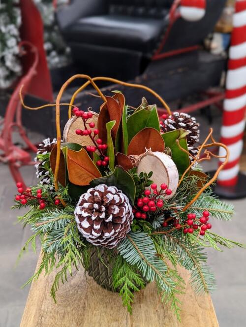 a green ceramic pot filled with festive greenery. featuring magnolia, fir, frosted pinecones, curly willow and red berries