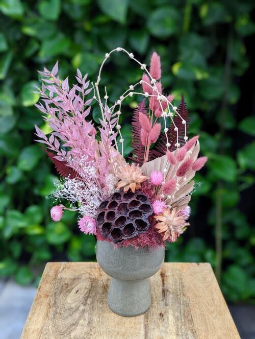 a grey pedestal ceramic with a mix of pink and purple dried florals and large lotus pod