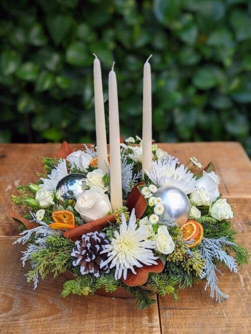 winter greenery with 3 white tapered candles, white mums, white spray roses, white roses and orange slices