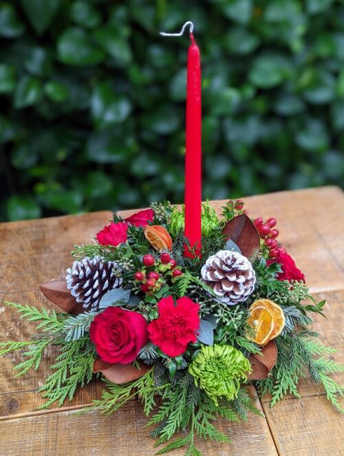 A bed of winter greenery with red roses, pincecones, green mums red hypericum and red carnations