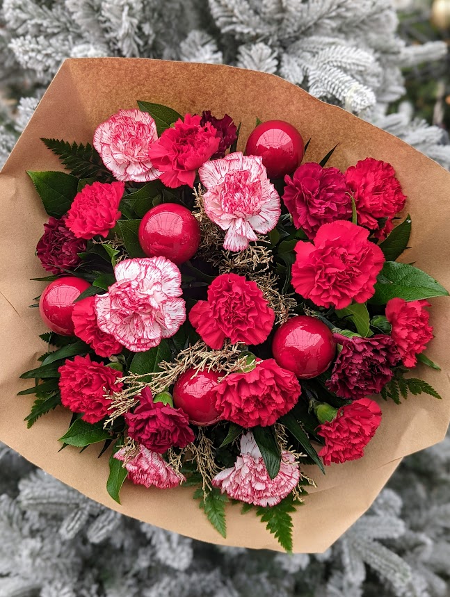 a red bouquet featuring a variety of carnations, burgundy red and candy cane with red ornaments