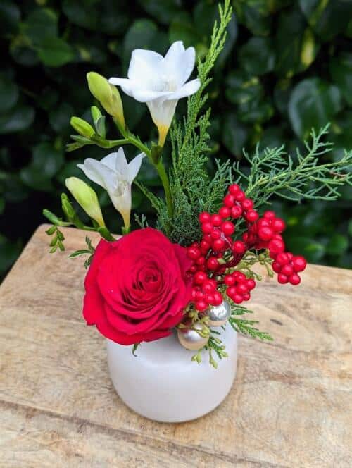 A beige matte bud vase with a red rose,white freesia, faux berries and winter greens