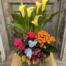 The Butterfly Oasis arrangement shown from the side, with yellow calla lilies rising above hot pink and orange blooms and a blue butterfly accent in a grey ribbed pot.