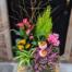 a dark green ceramic filled with pink and green plants accented with a yellow kalanchoe and moss. featuring lemon cypress, pink calla lilies, heather and more,