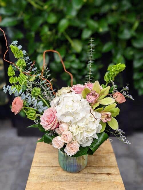 a ribbed iridescent vase filled with light pink, green and white blooms.