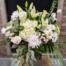 a clear textured vase filled with white and green flowers such as hydrangeas, lilies, mums and spray mums, accented with blue tweedia and seeded eucalyptus.