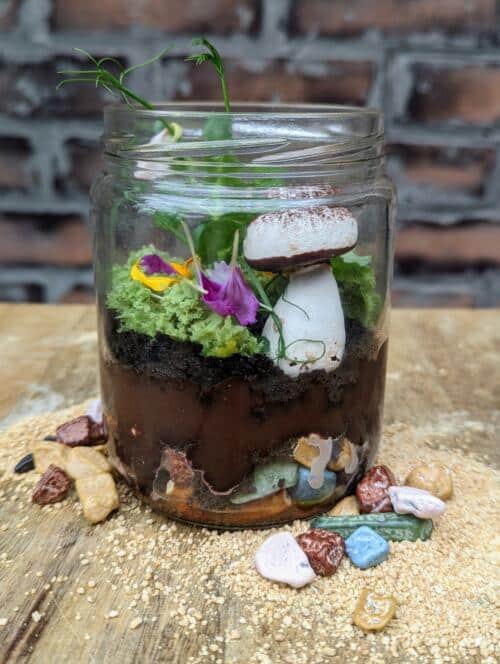 The Watering Can | This kit features an ediable terrarium made in a glass jar with layers of pretzels, chocolate pudding, cake, candy rocks and a meringue mushroom.